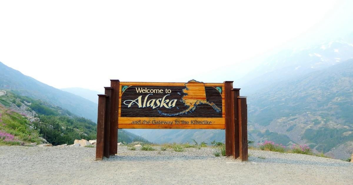 Welcome to Alaska sign stands on the edge of a mountain range