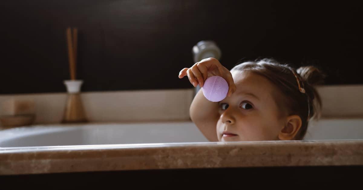 Young child in bath holding up a bath bomb