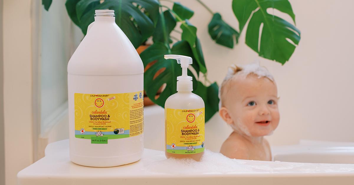 Baby in bathtub next to California Baby shampoo in two different sized bottles.