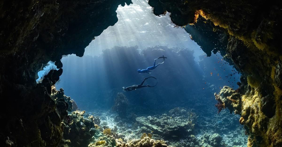 Two divers swim around a reef while the sun shines in the water