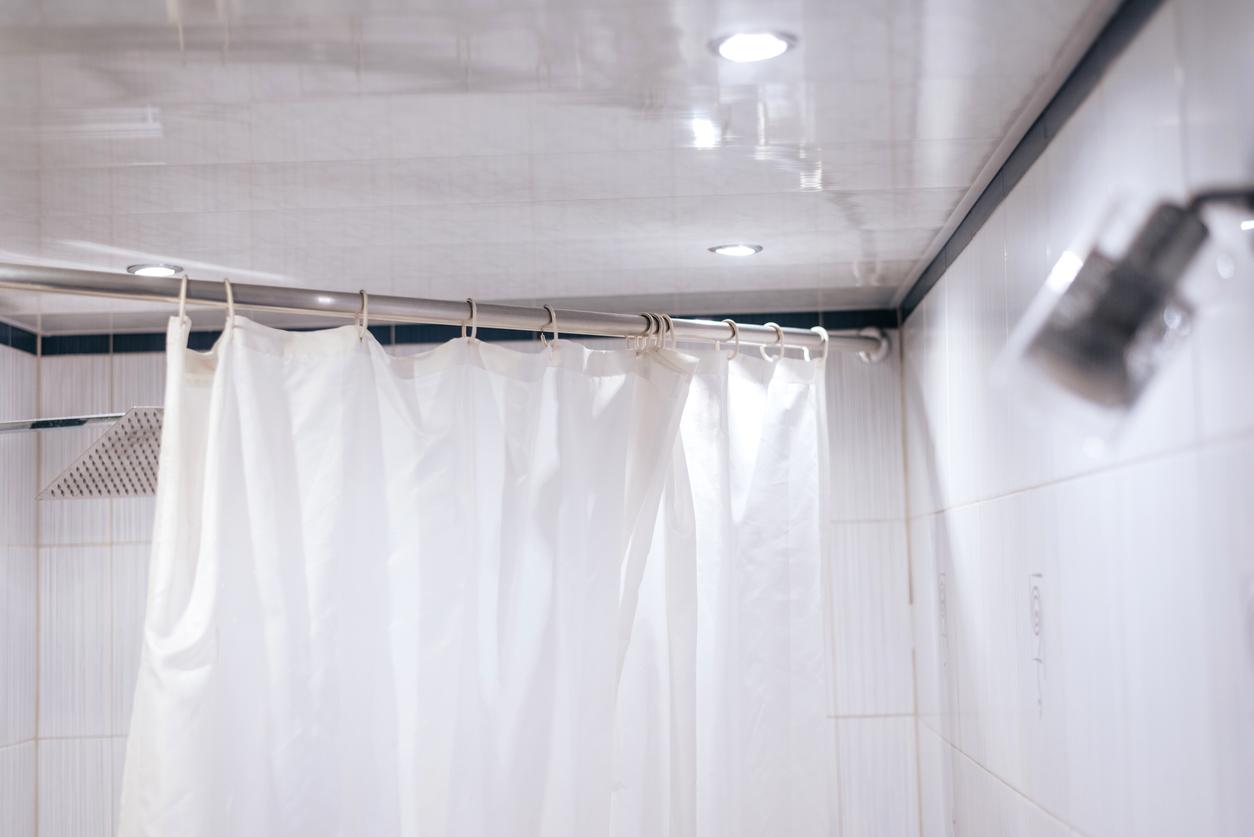 White shower curtain liner hanging on rod in a bathroom