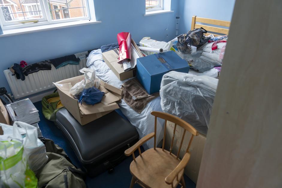 A bedroom that is full of items covering the bed and the floor. 