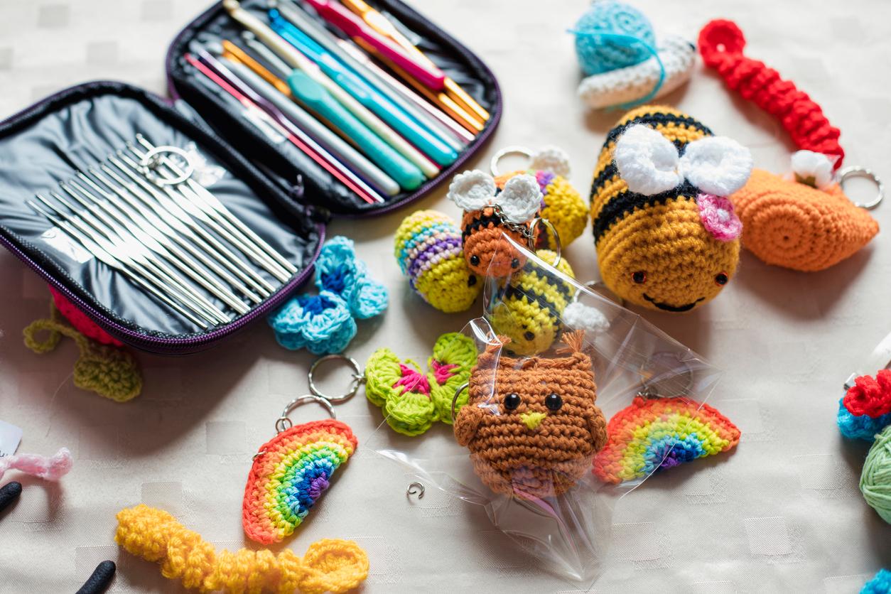 A kit full of different crochet hooks and tools surrounded by various crocheted figures like bees, rainbows, and butterflies.