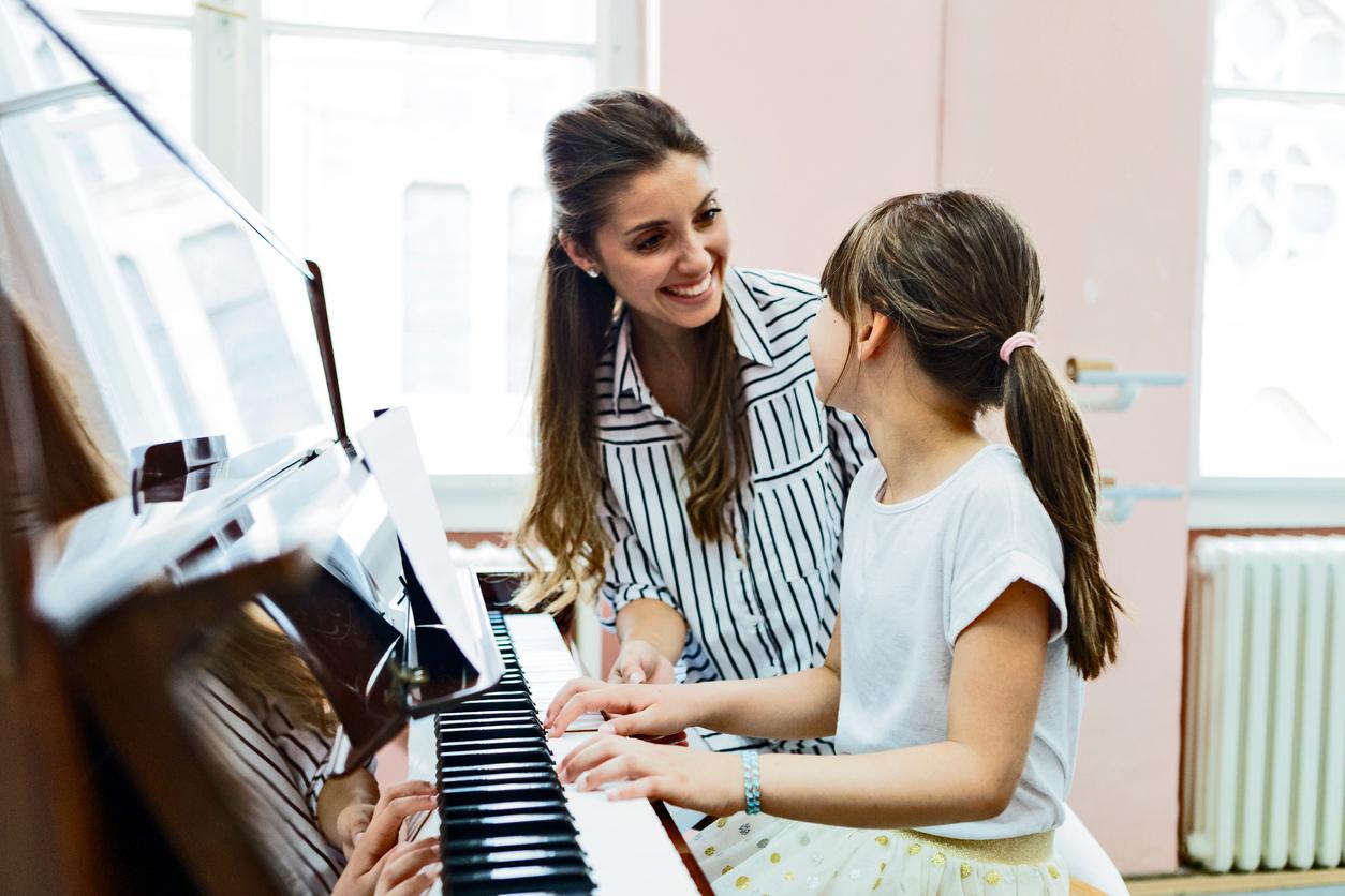A music teacher smiles at a student in school while she plays on a donated piano.