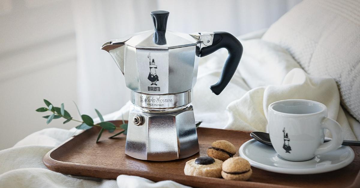 Product photo of the Bialetti Moka Pot on a serving tray beside a mug and cookies
