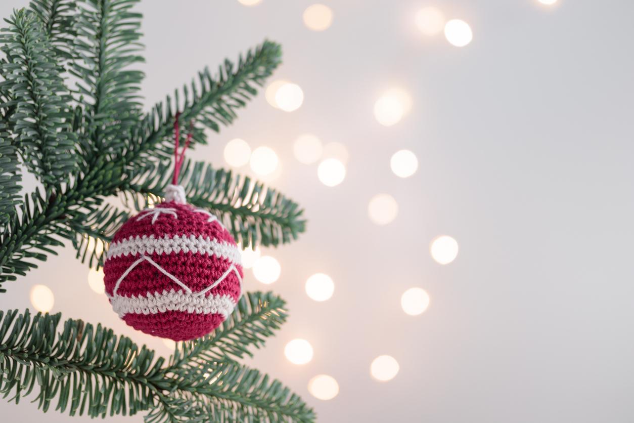 A close up view of a red and white crocheted ornament hanging from a Christmas tree.