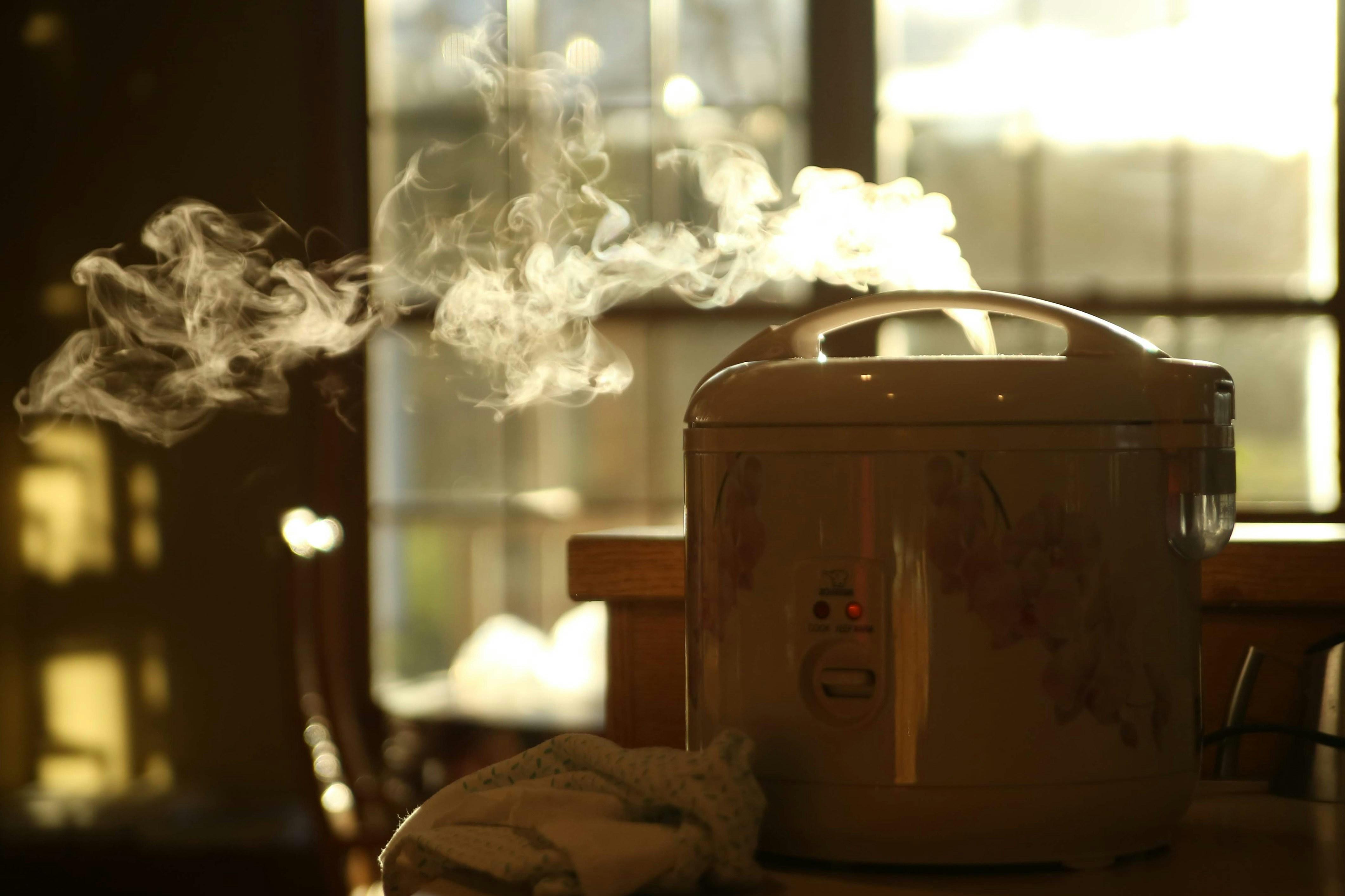 A pressure cooker is pictured atop a table with steam being dispersed into the air.