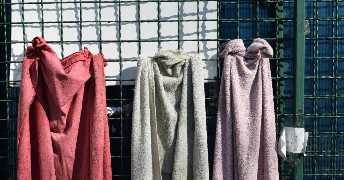 Three bath towels are hung up on a fence to dry