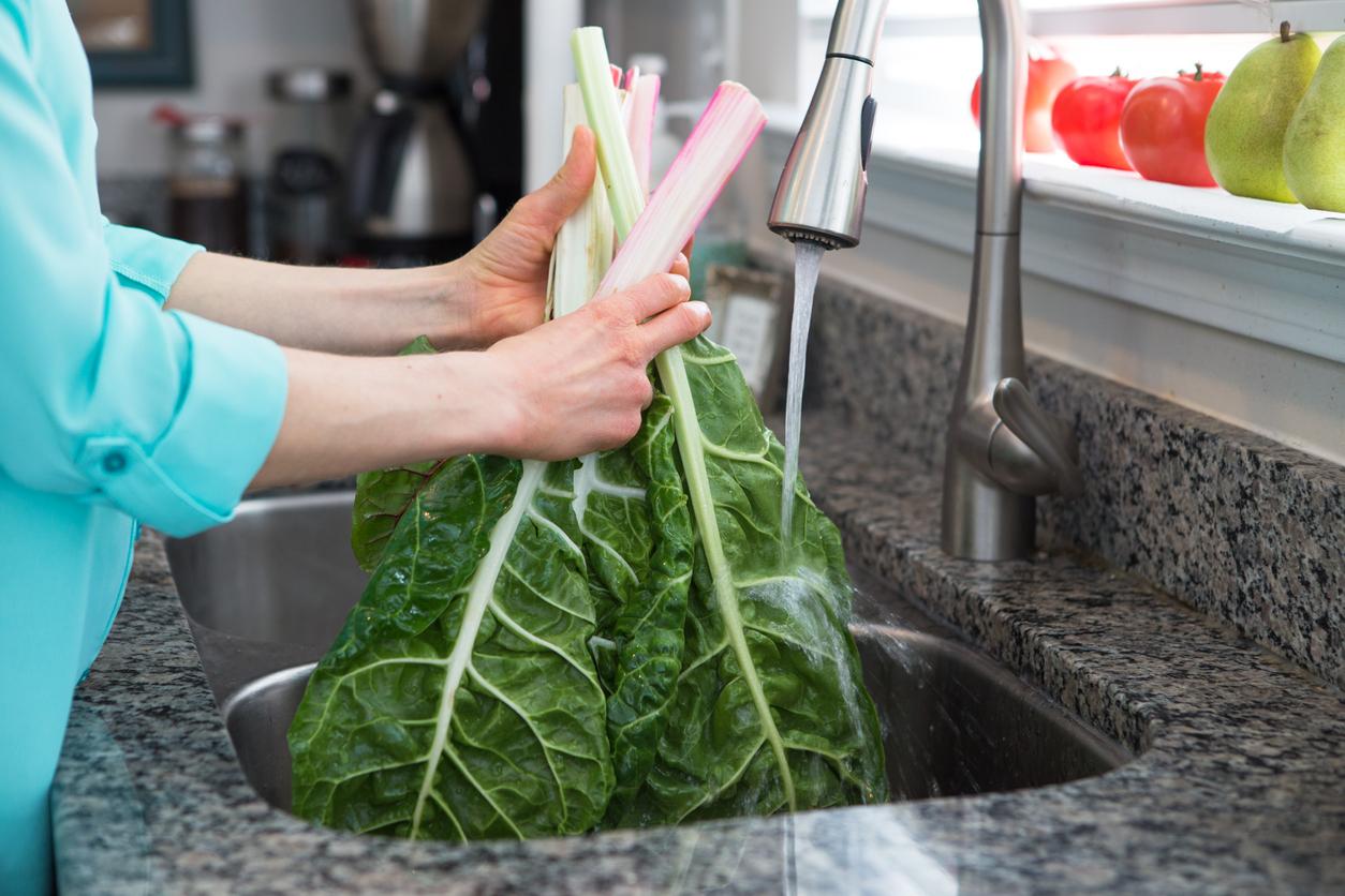 A woman wearing a blue shirt washes collard greens in a kitchen sink.