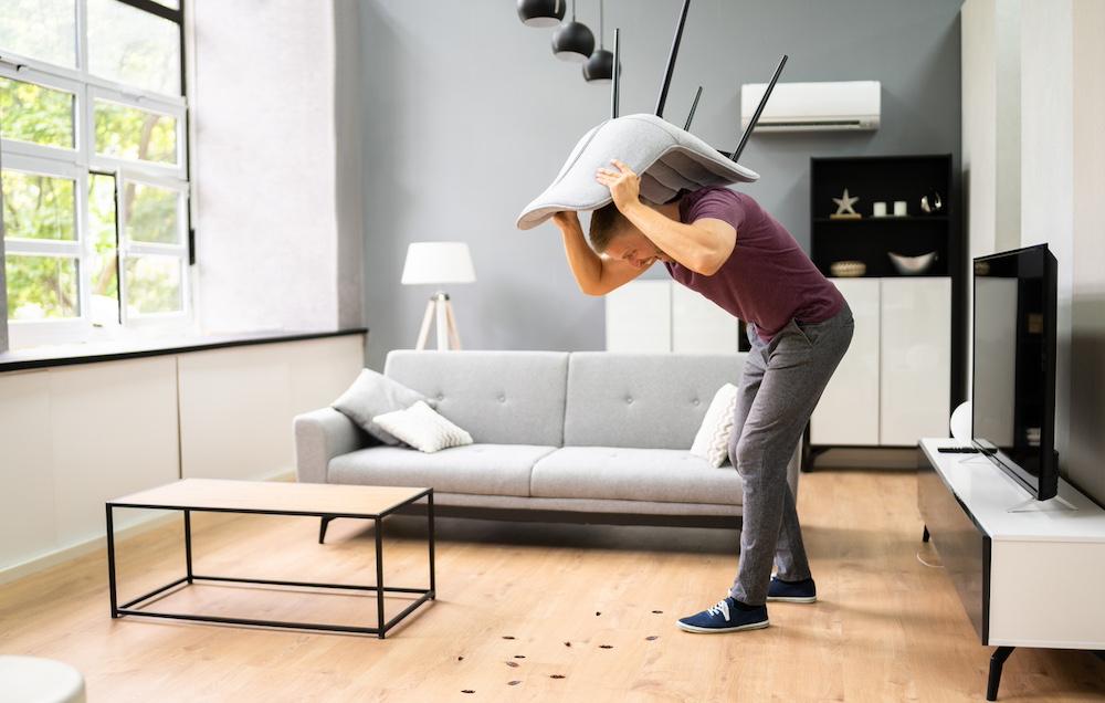 A man discovering roaches under a chair in a living room. 