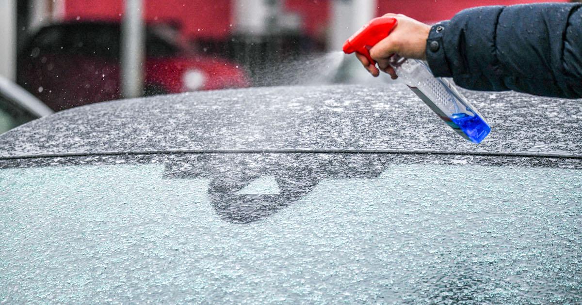 Hand sprays a spray bottle onto an icy windshield