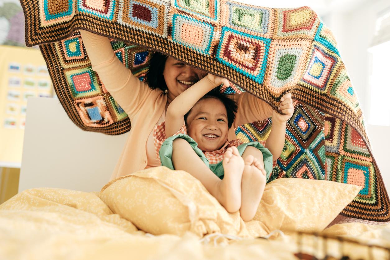An mother and her child playing with a crochet blanket.