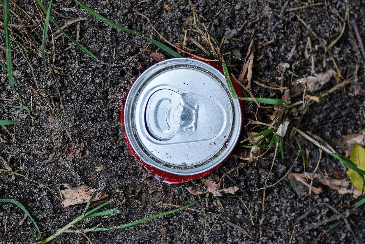An overhead view of a beer can in the dirt outside.