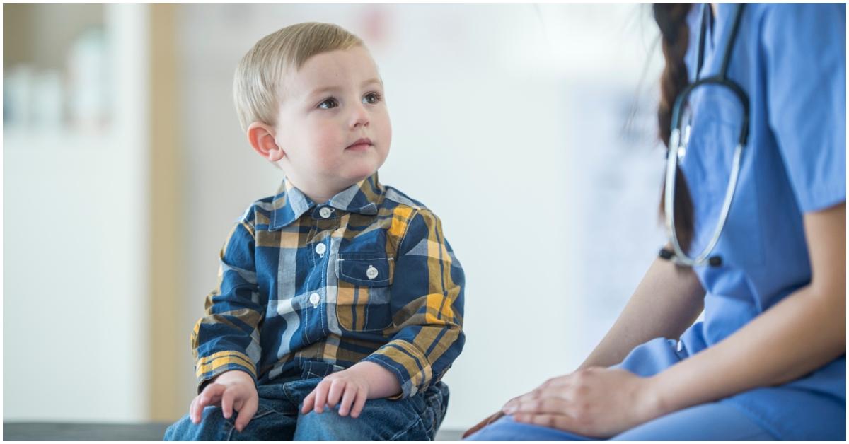A young boy sits on an examination table while looking up at the doctor. 