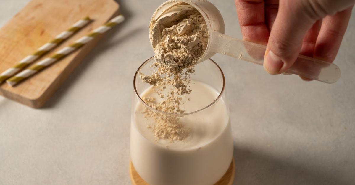 A person pours a scoop of protein powder into a glass of milk.