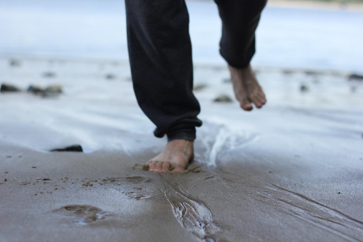 person in black pants walking barefoot on wet sand