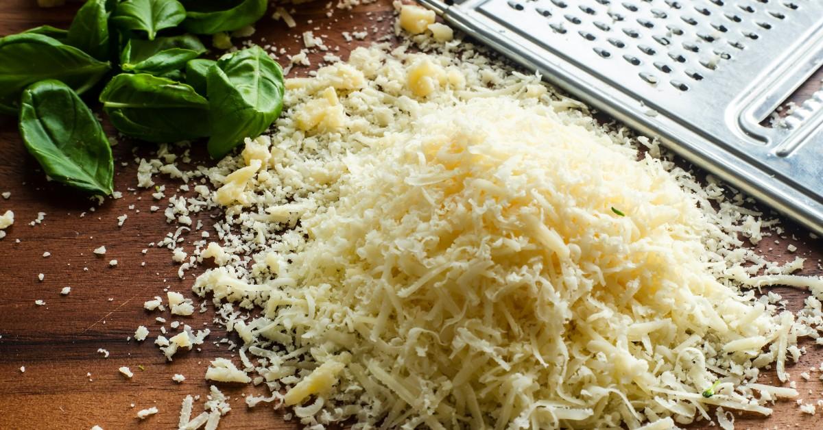 Shredded cheese sits piled up next to a cheese grater 