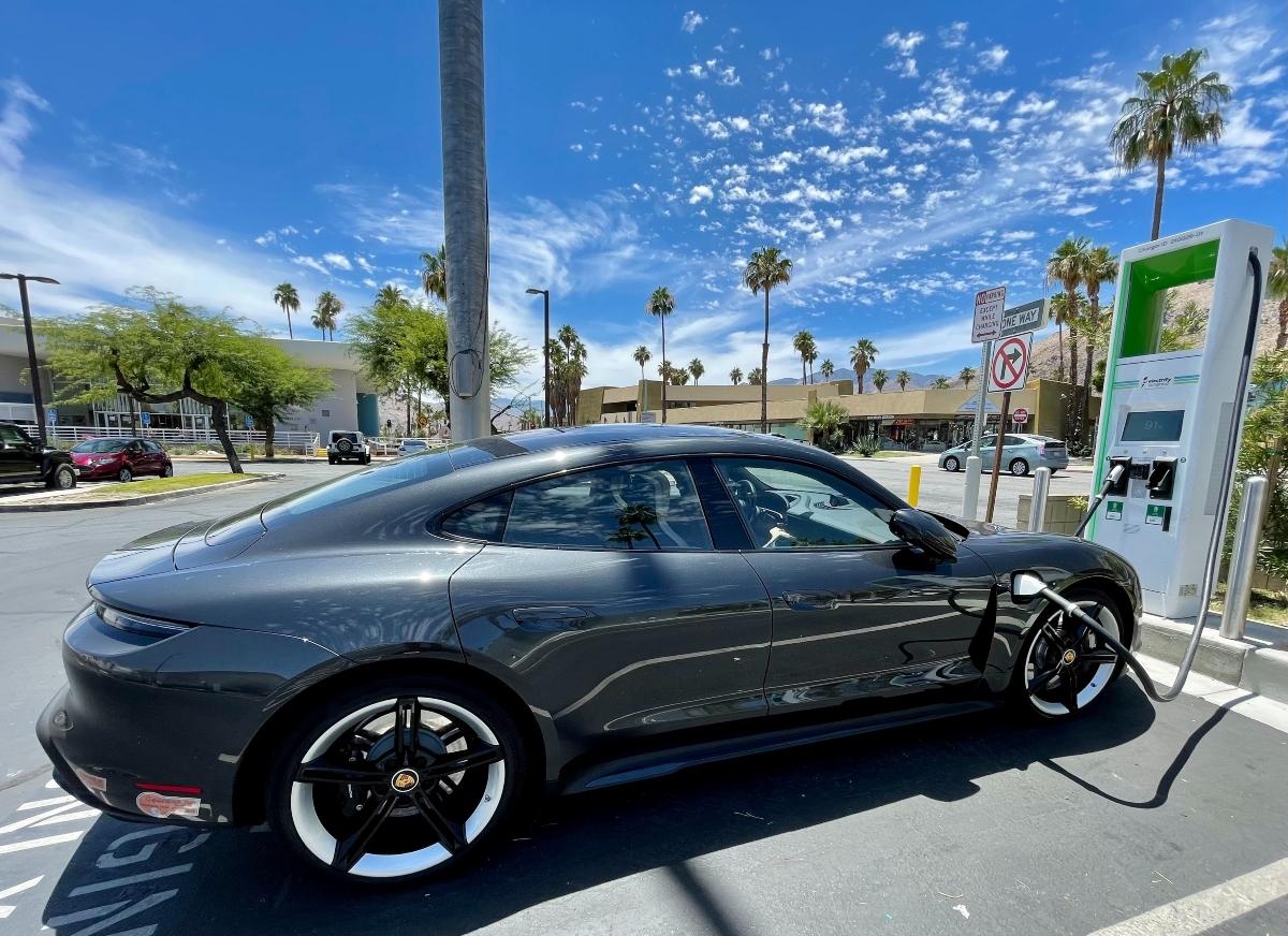 black EV Porsche at charging station with palm trees surrounding