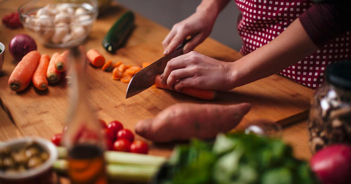 A person chops a carrot on a butcher block, alongside various other raw vegetables.