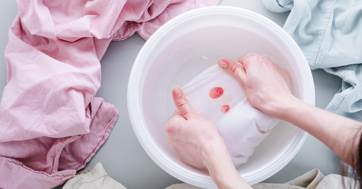 A woman scrub stains out of her clothes using a mix of laundry cleansers 