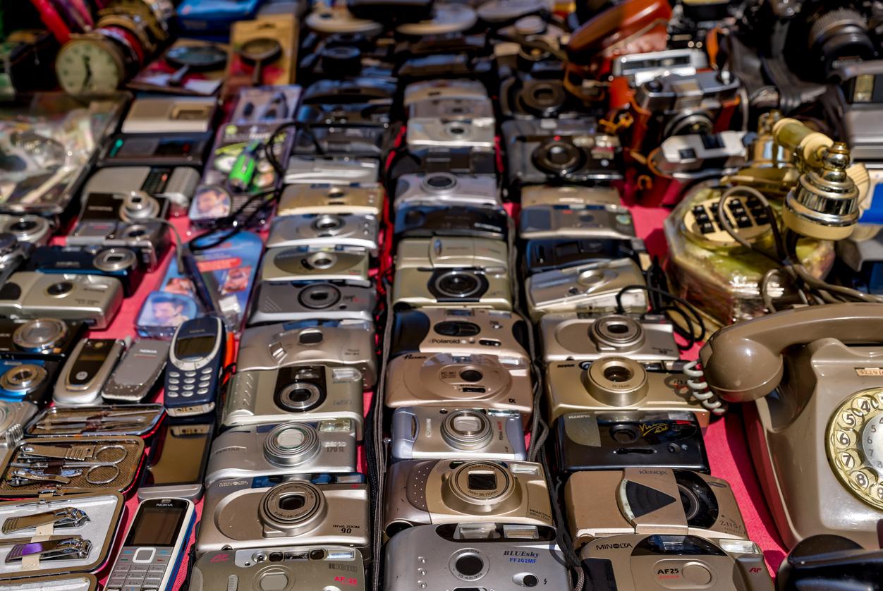 A large variety of vintage digital cameras and phones from the early 2000s spread out on a table.