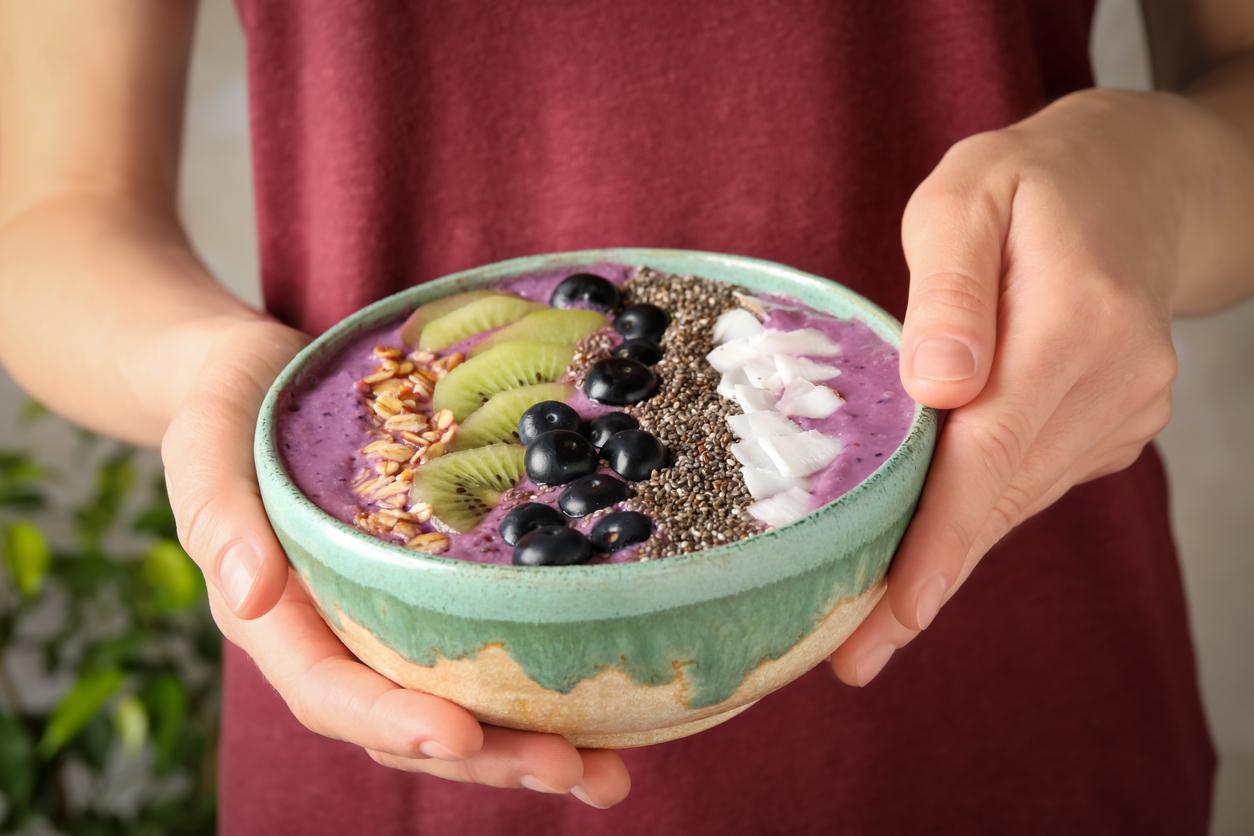 A woman in a red top holds an açaí smoothie bowl with fruit inside.