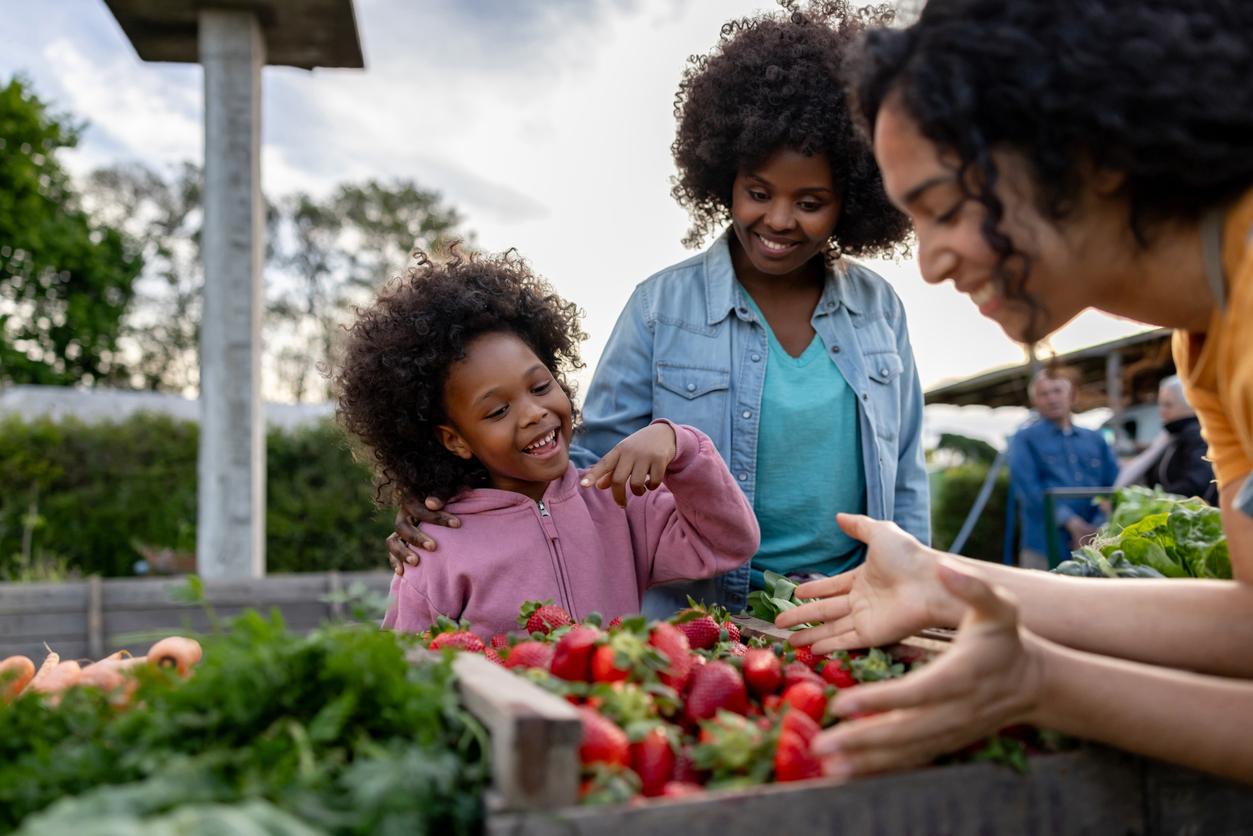 A smiling young girl and her mom purchase strawberries from a smiling farmers market vendor.