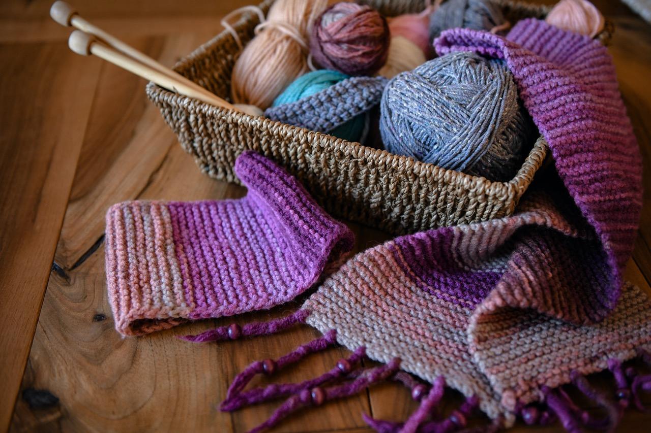 A woven basket full of yarn and knitting needles on a table.