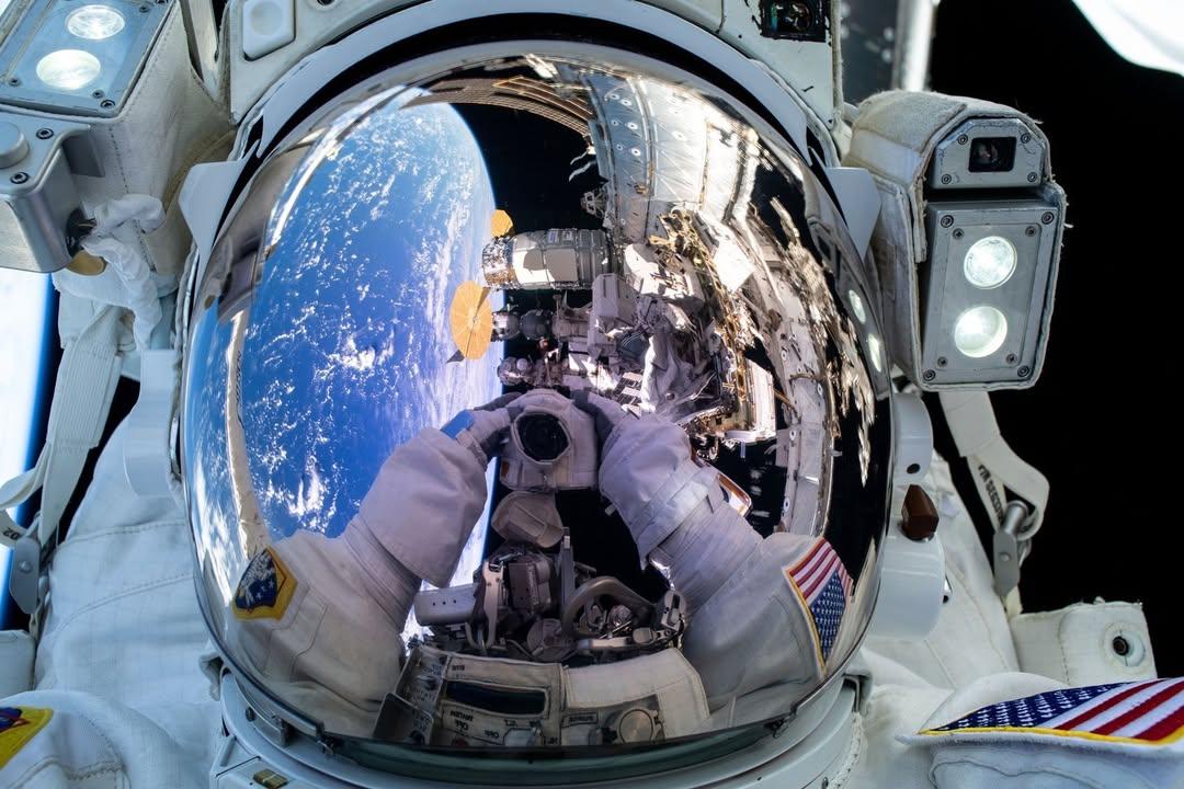 Astronaut Suni Williams takes a selfie above the Pacific Ocean with the International Space Station partially in view in the reflection of her helmet.