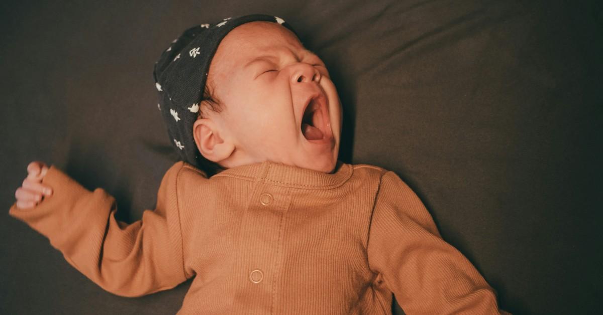 A sleepless baby yawns while laying down in bed