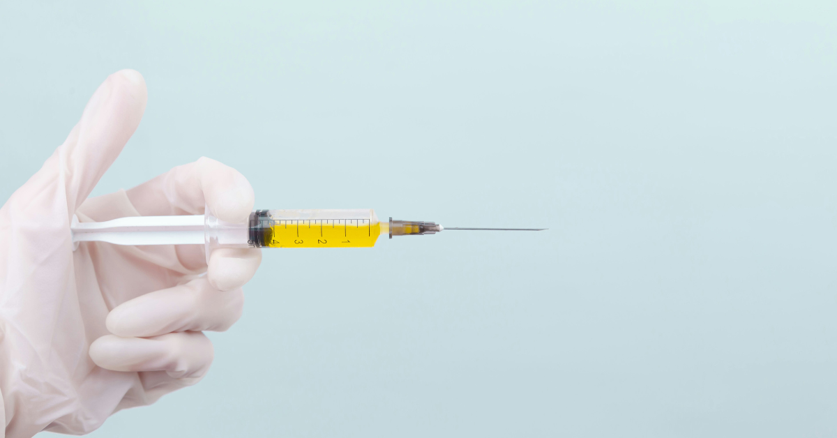 A gloved hand holds a yellow syringe 