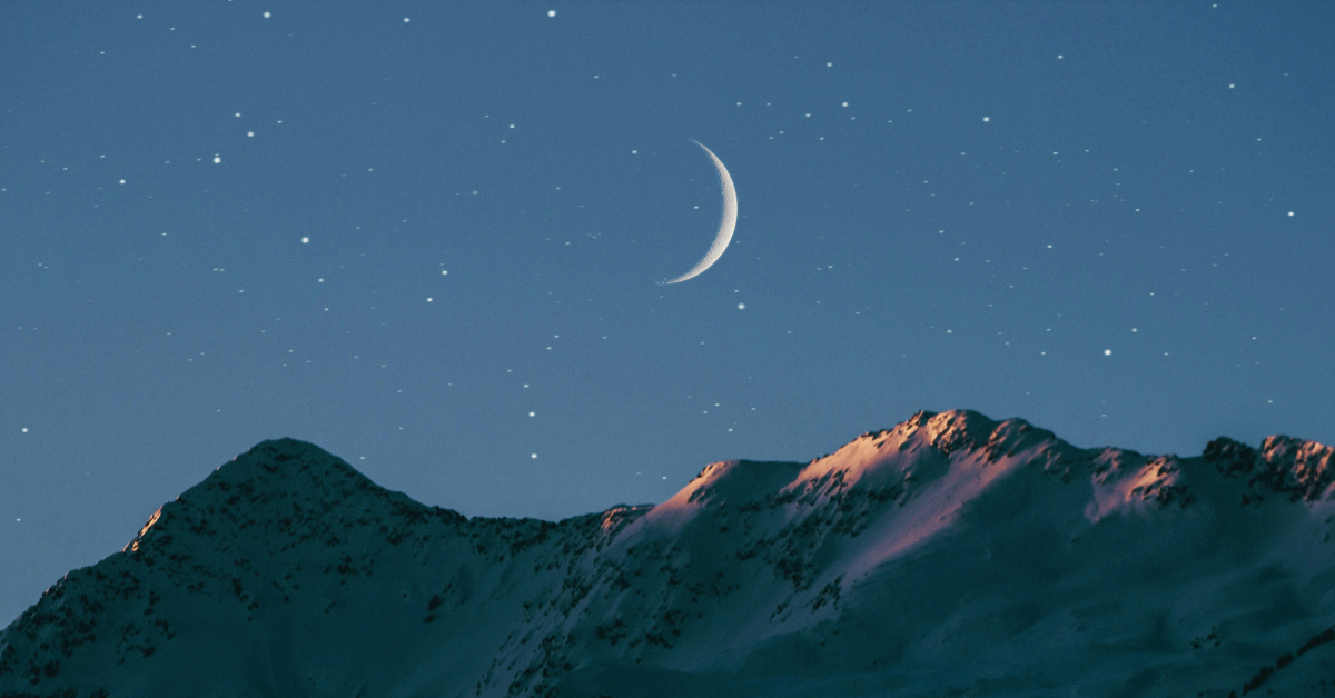 A crescent moon hangs above the mountains