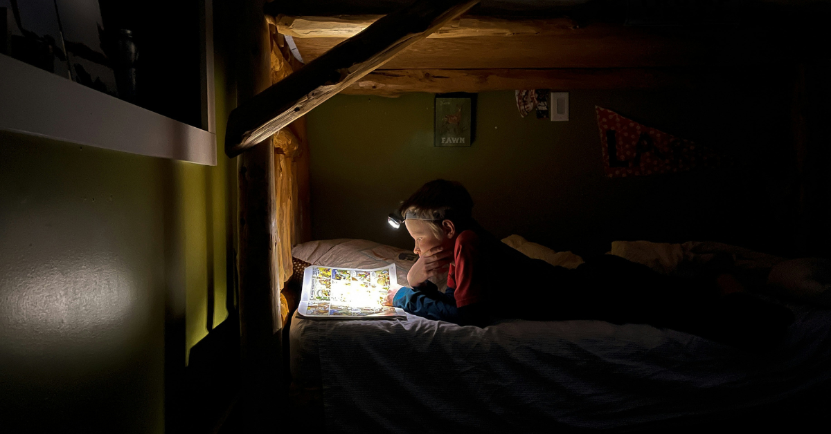 A child uses a headlamp to read at night instead of sleeping